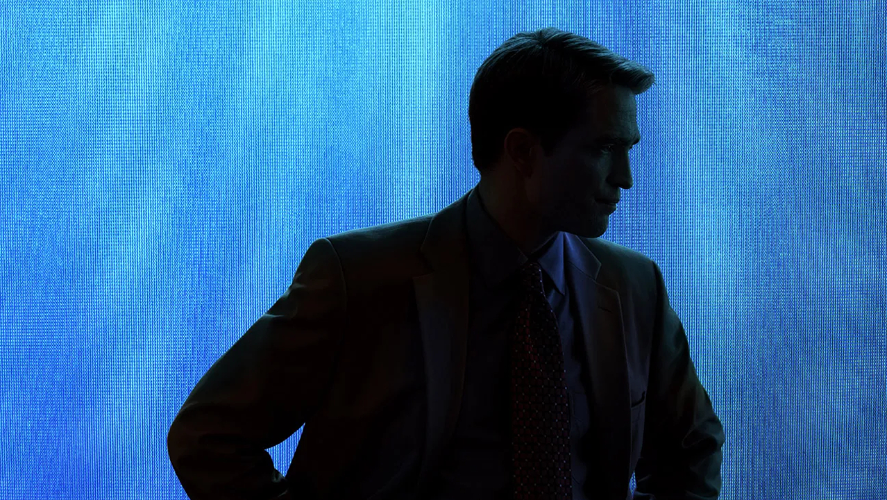 A man in a suit stands in shadow against a vivid blue screen in Primetime